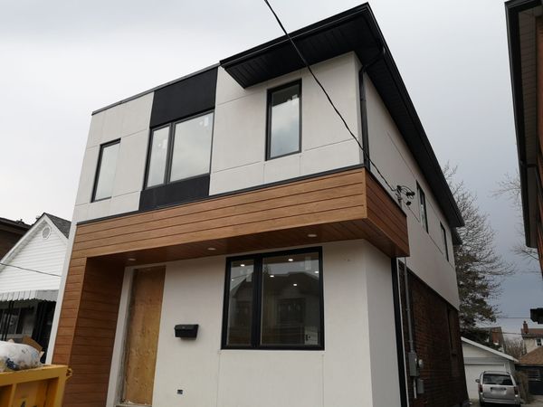 A two storey house with white panel cladding, black window frames, a wood clad overhang above the entrance and a black fascia