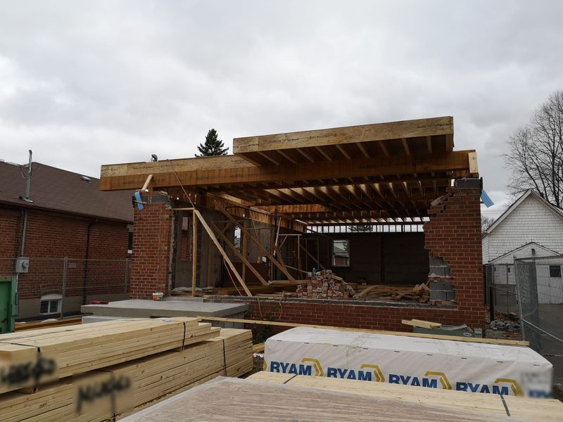 Floor joists against a brick wall, with lumber stacked in front