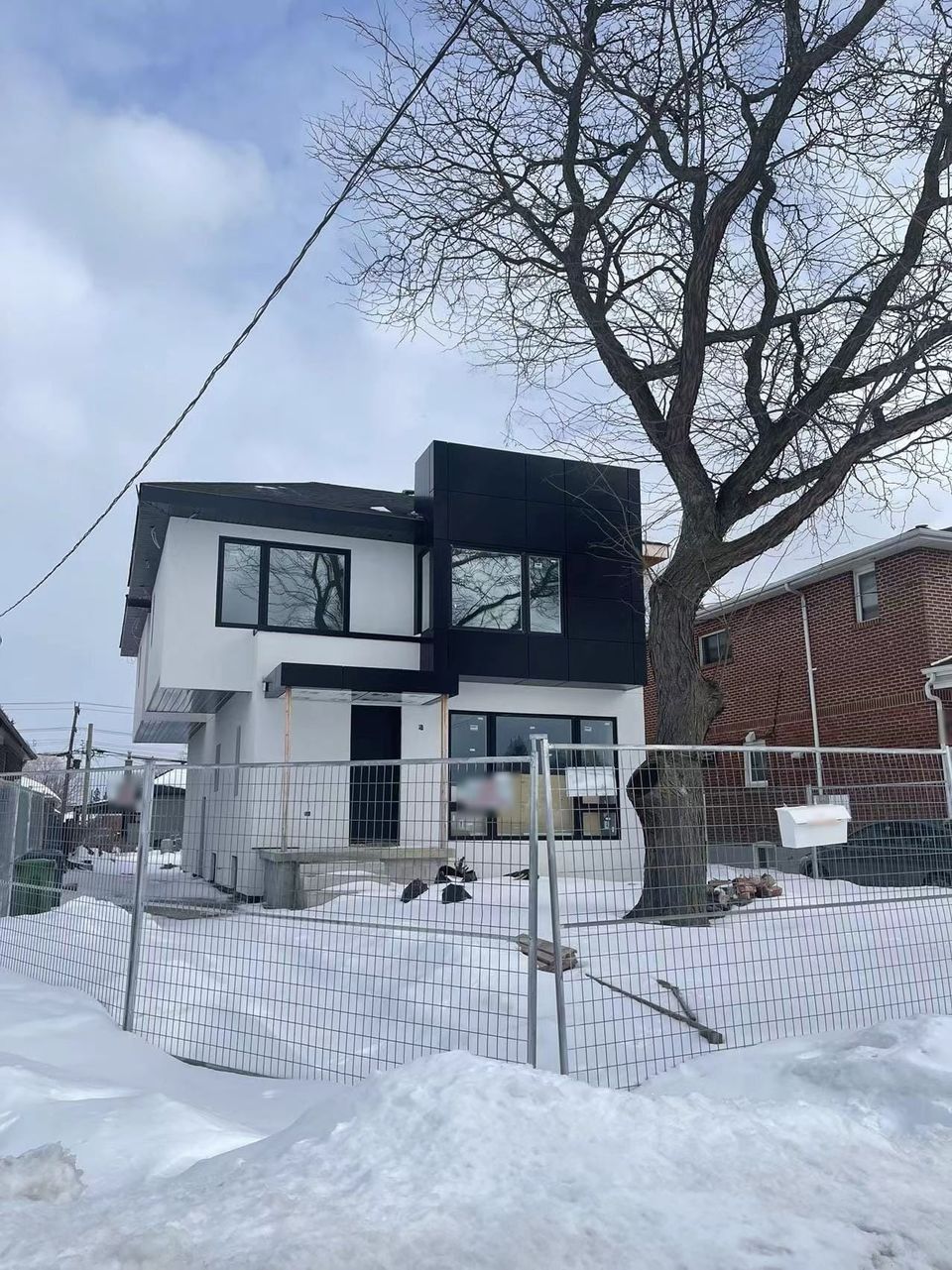 A house in winter with a white upper storey, a black clad box, black window frames and a canopy over the door