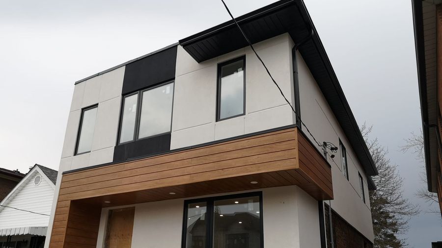 A two storey house with white panel cladding, black window frames, a wood clad overhang above the entrance and a black fascia