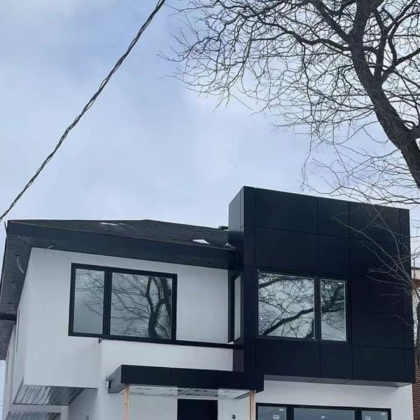 A house in winter with a white upper storey, a black clad box, black window frames and a canopy over the door