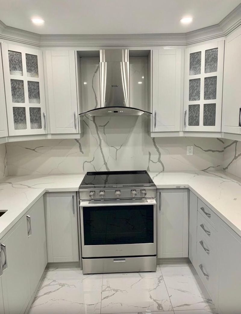 White U-shaped kitchen with a quartz slab backsplash, chimney range hood and marble-look tile floor