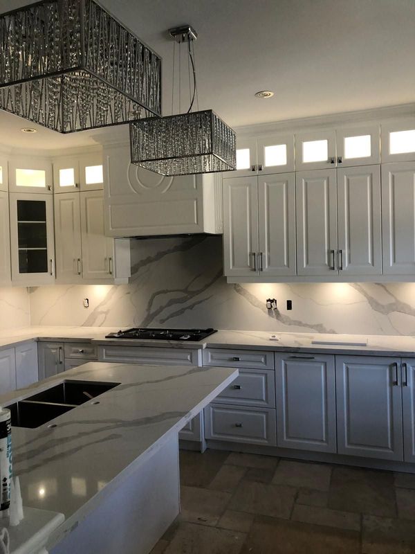 White kitchen with a quartz island, gas cooktop, slab backsplash and under-cabinet lighting