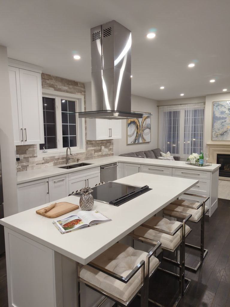 White shaker kitchen with a quartz island, stacked stone backsplash and island range hood