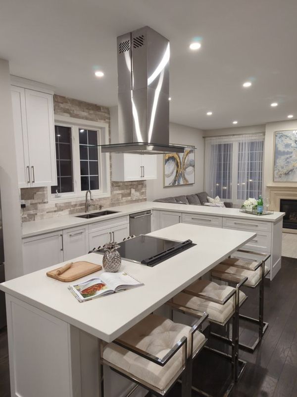 White shaker kitchen with a quartz island, stacked stone backsplash and island range hood