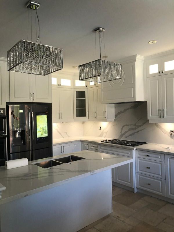 White kitchen with a quartz island, two crystal pendants and a full-height marble-look backsplash