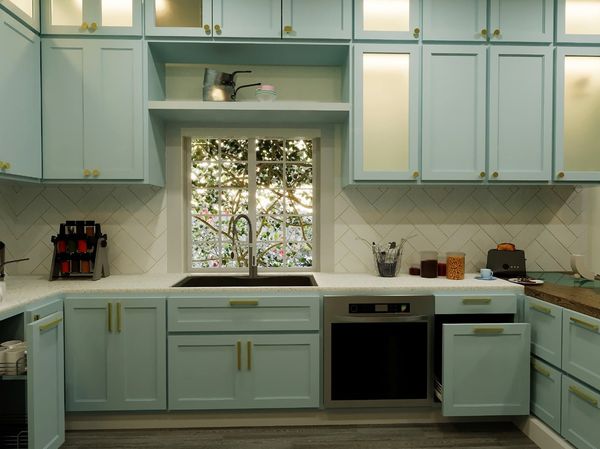 Rendering of a kitchen sink under a window, with pale blue cabinets and a herringbone backsplash, Brampton