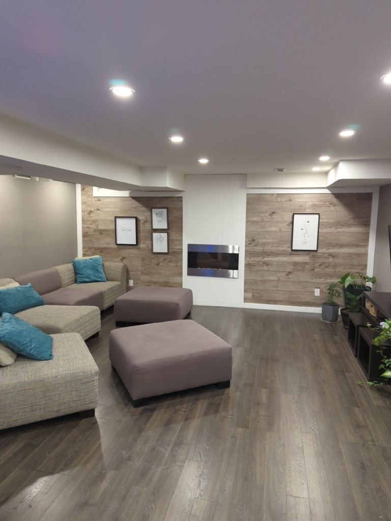 Finished basement with wood-look plank accent walls, an electric fireplace and pot lights