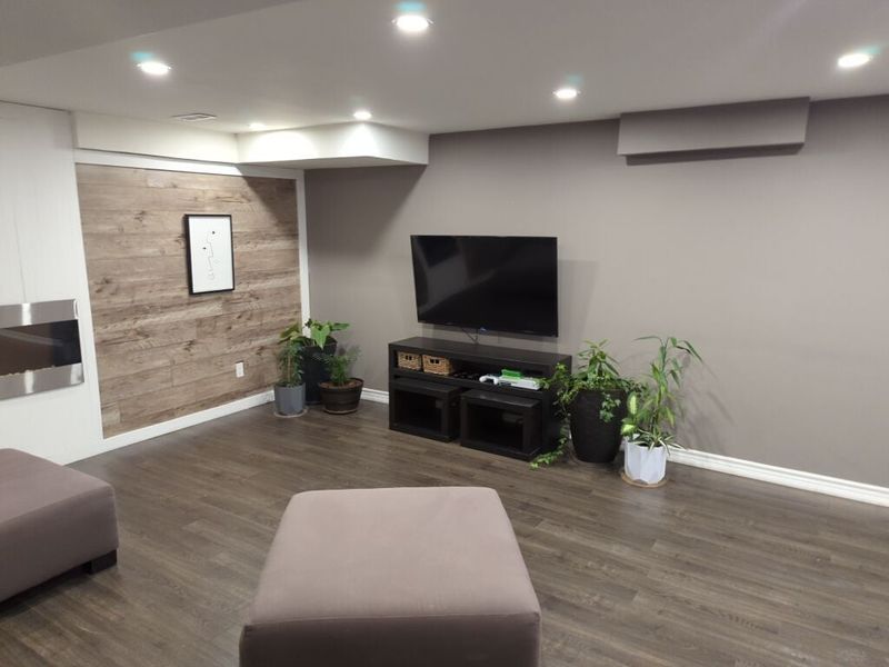 Basement media wall in grey beside a wood-look accent wall, with pot lights and laminate floor