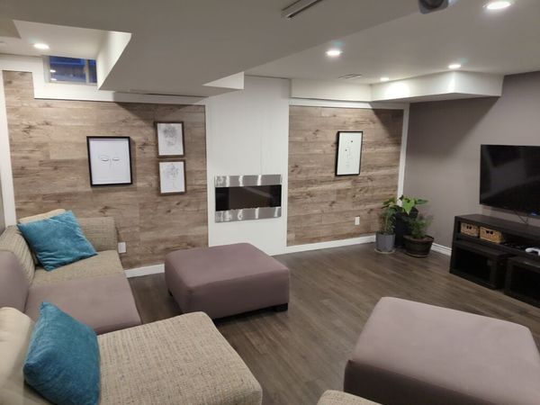 Finished basement with wood-look accent walls, an electric fireplace and pot lights