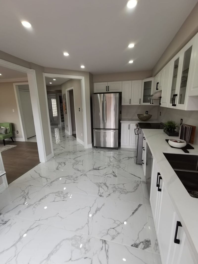 White kitchen opening to a hallway with large marble-look porcelain tile and pot lights