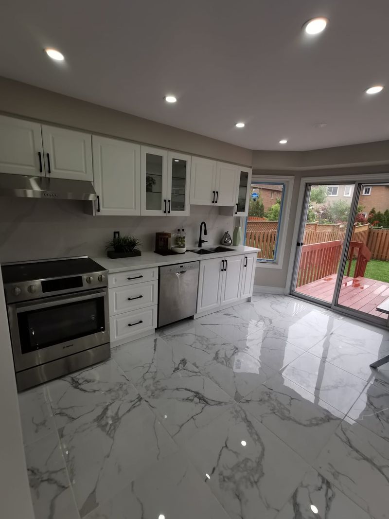 White kitchen with black hardware, quartz counters and glossy marble-look floor tile