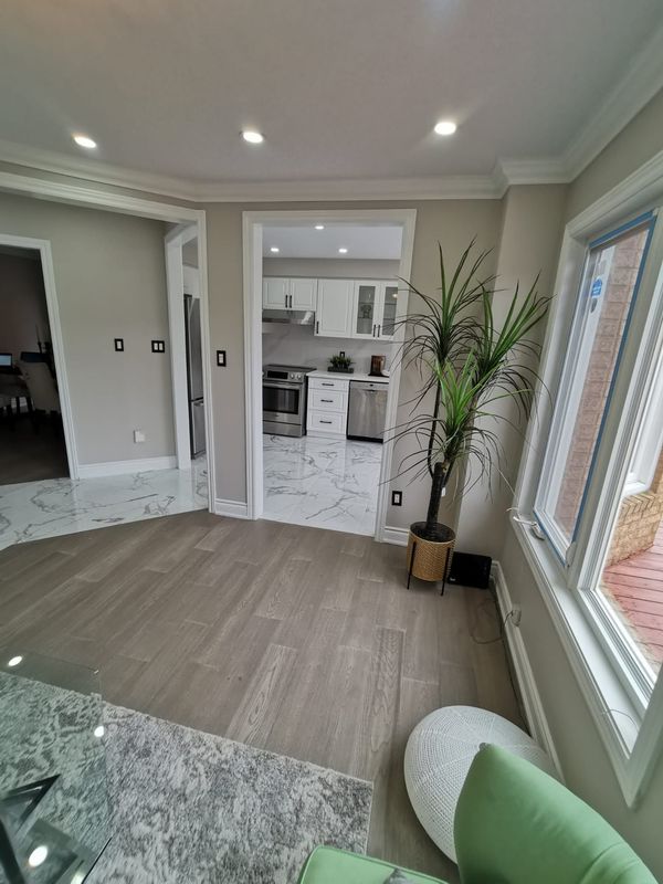 Sitting area with grey wood-look flooring meeting marble-look tile at the kitchen doorway