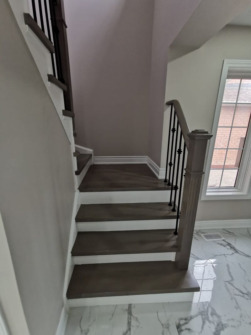 Stained stair treads with white risers, wrought iron spindles and a grey newel post