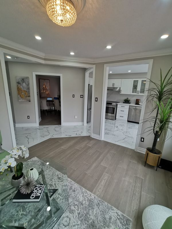 Open main floor with grey wood-look flooring, marble-look tile, crown moulding and pot lights