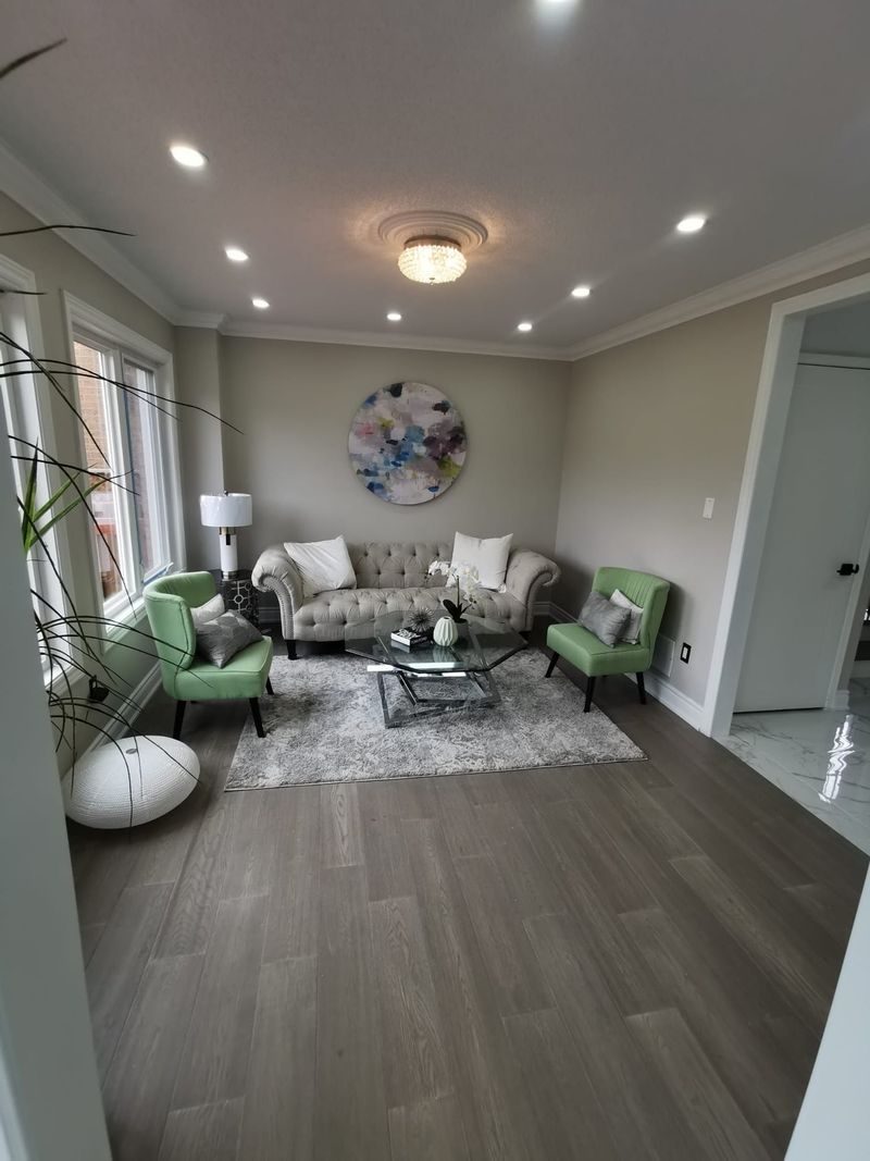 Living room with grey wide-plank flooring, crown moulding, pot lights and a crystal fixture