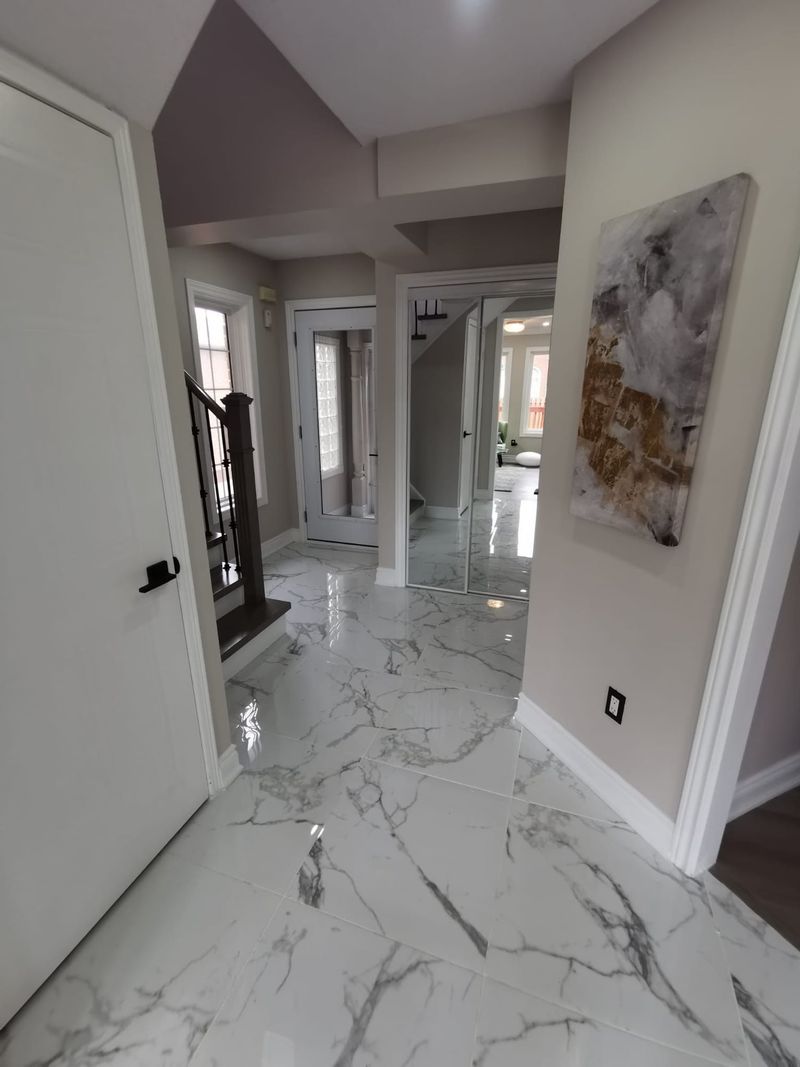 Front foyer with large marble-look porcelain tile, mirrored closet doors and stained stairs