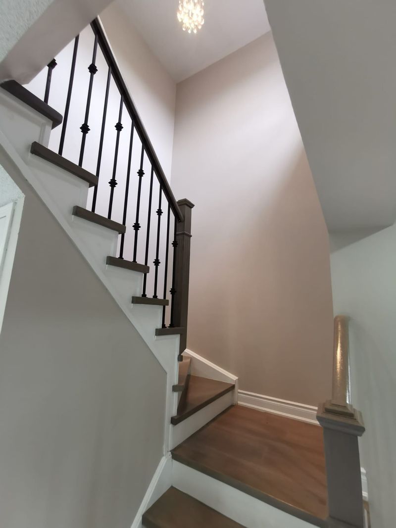 Staircase with stained treads, white risers and wrought iron spindles under a pendant light