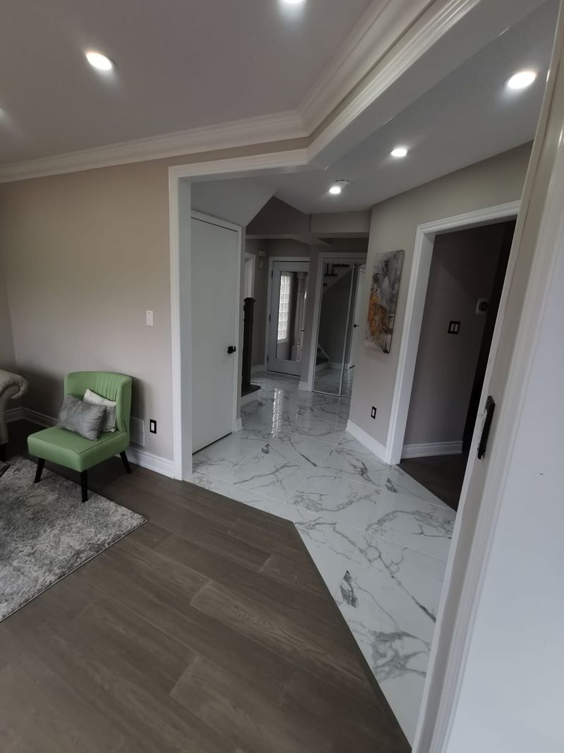 Living room and hallway with grey wood-look flooring meeting marble-look porcelain tile