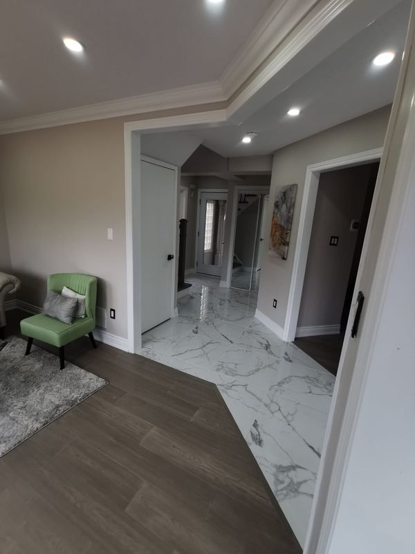 Living room and hallway with grey wood-look flooring meeting marble-look porcelain tile