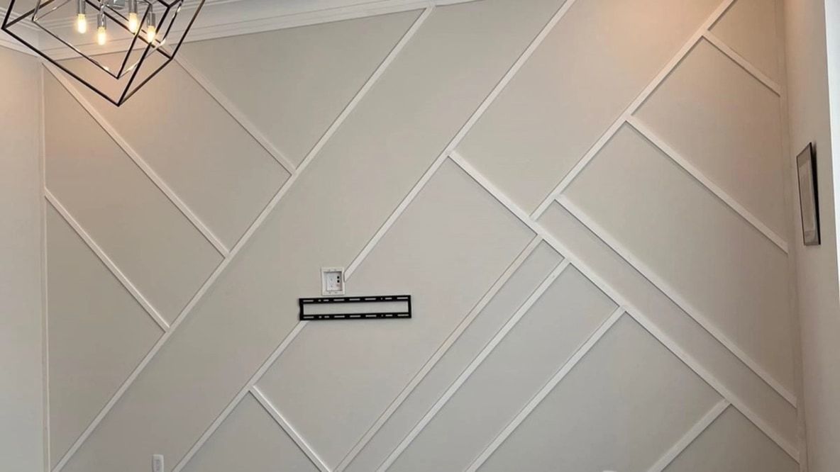 Living room accent wall with white diagonal trim panels, crown moulding and cube chandelier