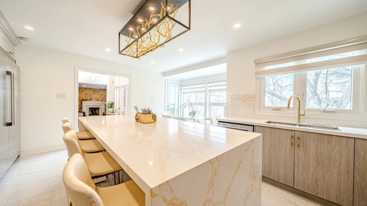 Kitchen with a gold veined quartz waterfall island, cream bar stools, grey wood grain cabinets and a brass faucet
